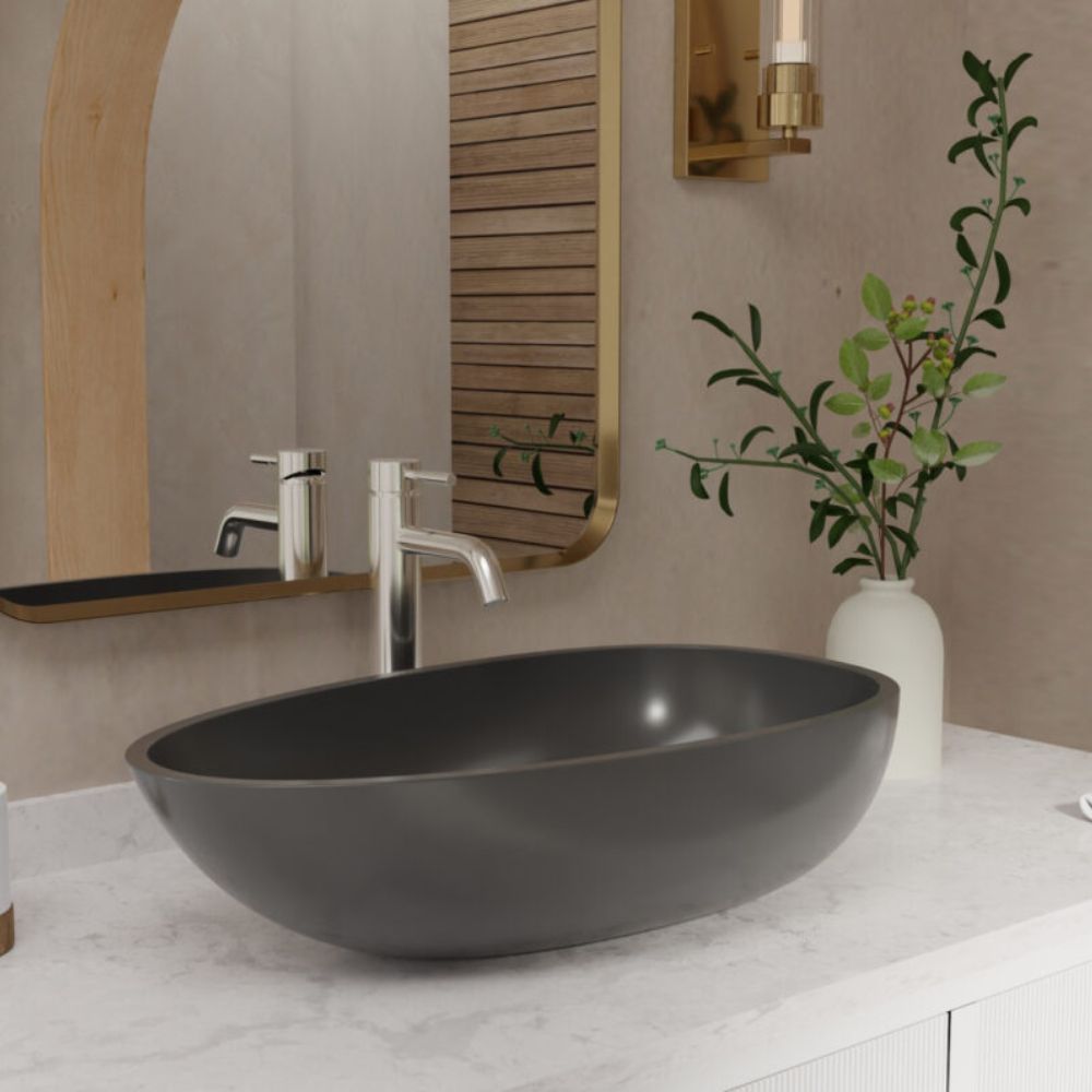 A matte black oval vessel sink basin set into a white marble bathroom countertop, paired with a polished chrome faucet, a gold-framed mirror, and a white vase with green leaves on a beige wall.