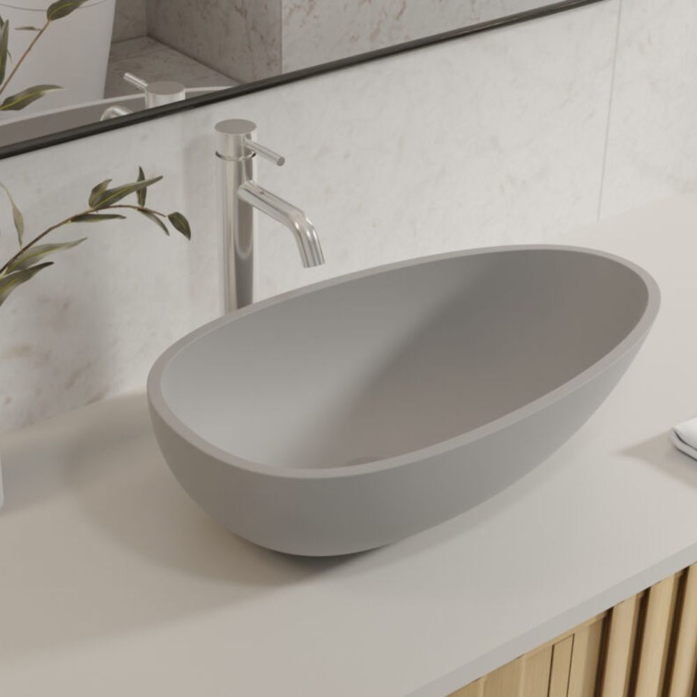 A modern oval gray vessel sink basin with a chrome faucet, set on a white countertop against a light marble-look tiled wall.