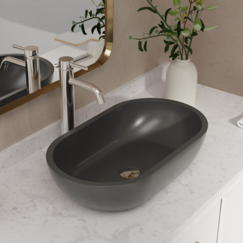 A matte black oval vessel sink basin installed on a white marble bathroom countertop, shown with a chrome faucet and a mirror in a styled bathroom setting.