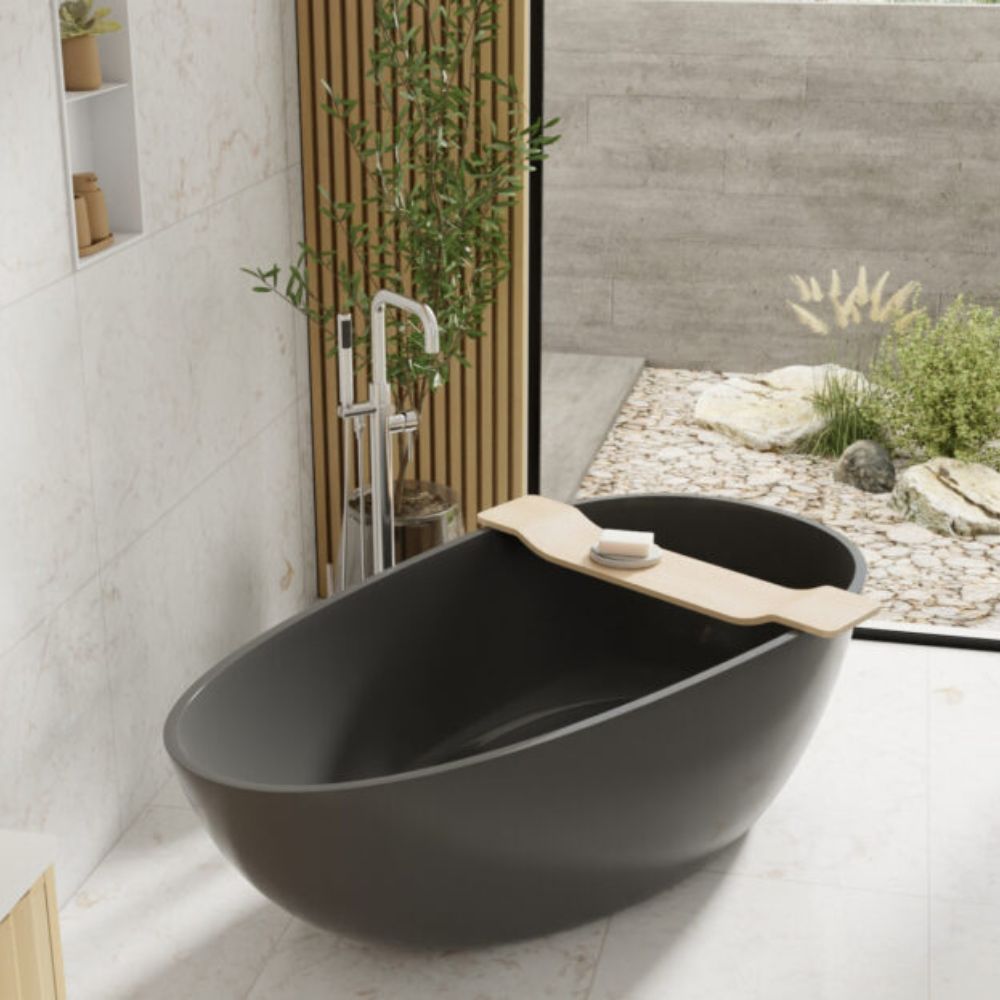 A modern freestanding oval bathtub in matte black with a light wood insert along the rim, shown in a styled bathroom setting with a chrome faucet, tiled walls, and an outdoor garden view.