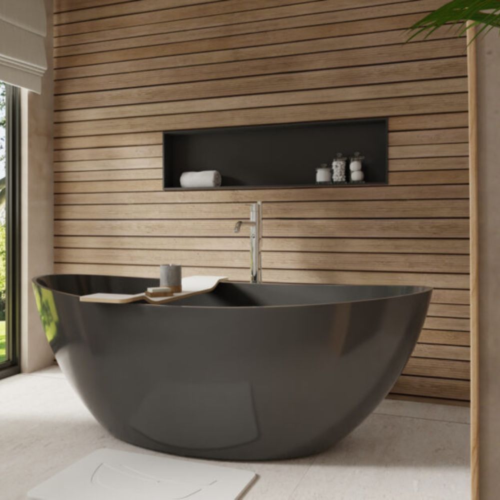 A modern freestanding oval bathtub in dark charcoal gray, set in a bathroom with a light wood slat wall, recessed shelf, and a chrome faucet.
