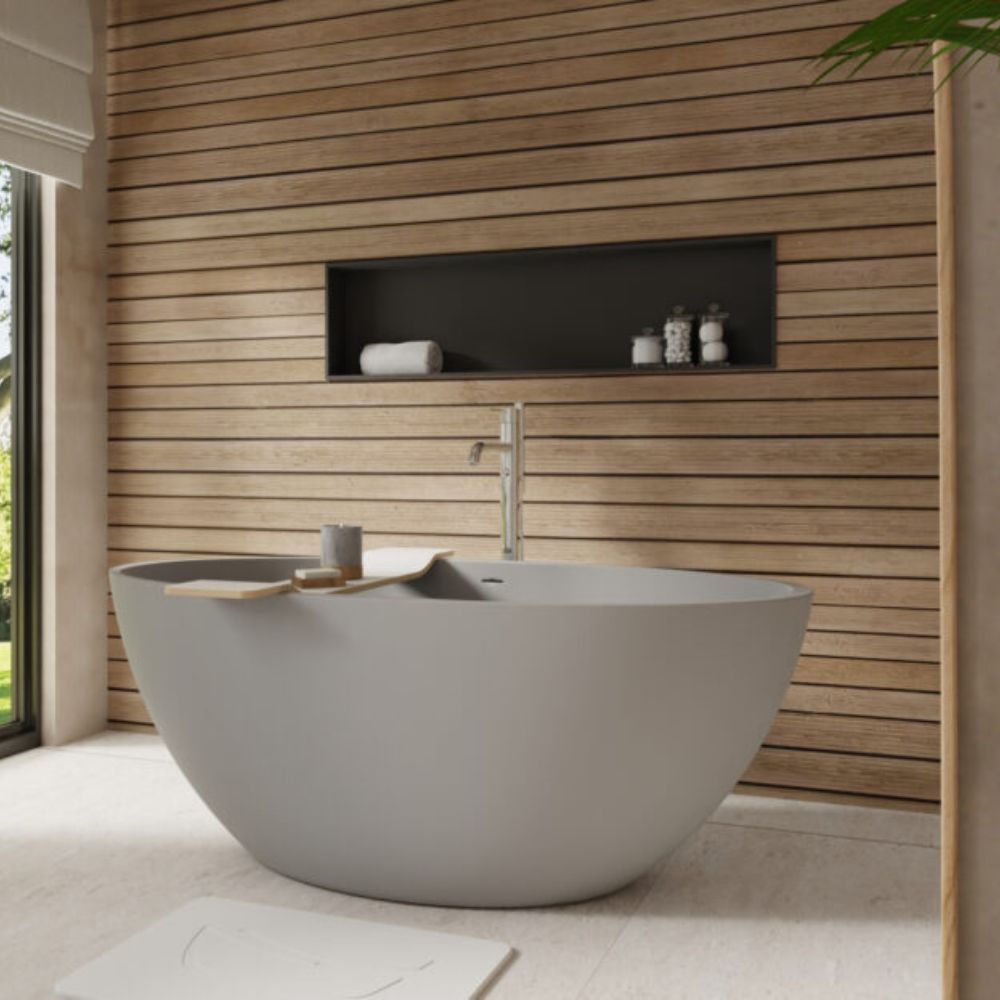 A modern freestanding oval bathtub in matte light gray, set in a bathroom with a wood slat wall, recessed shelf, and a wall-mounted chrome faucet.