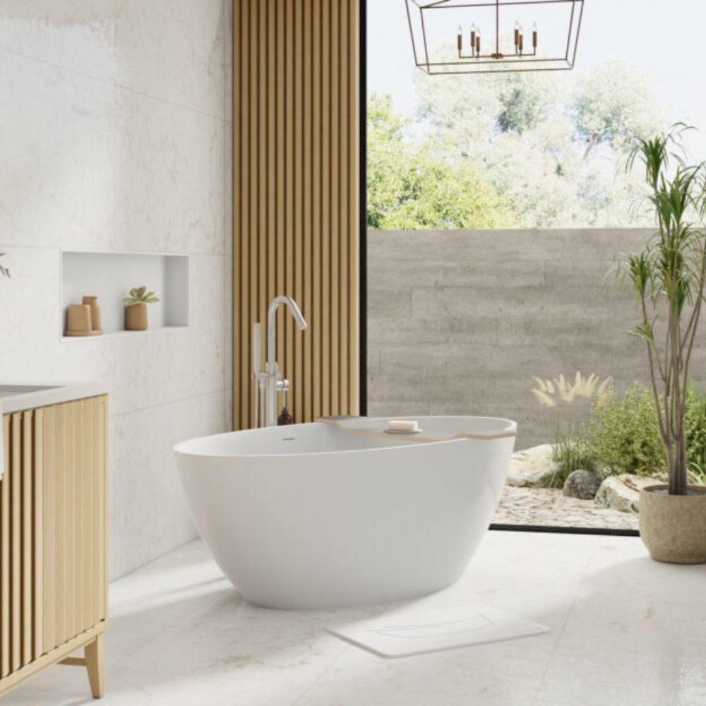 A modern freestanding oval bathtub in white with a chrome faucet, placed in a bright bathroom with light wood slat walls and a large window overlooking a garden.