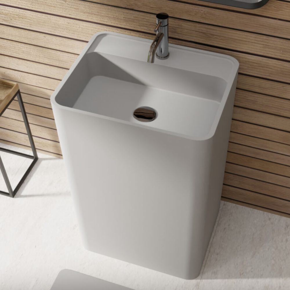 A modern rectangular pedestal bathroom sink in matte white, paired with a chrome faucet, set against a light wood slat wall.