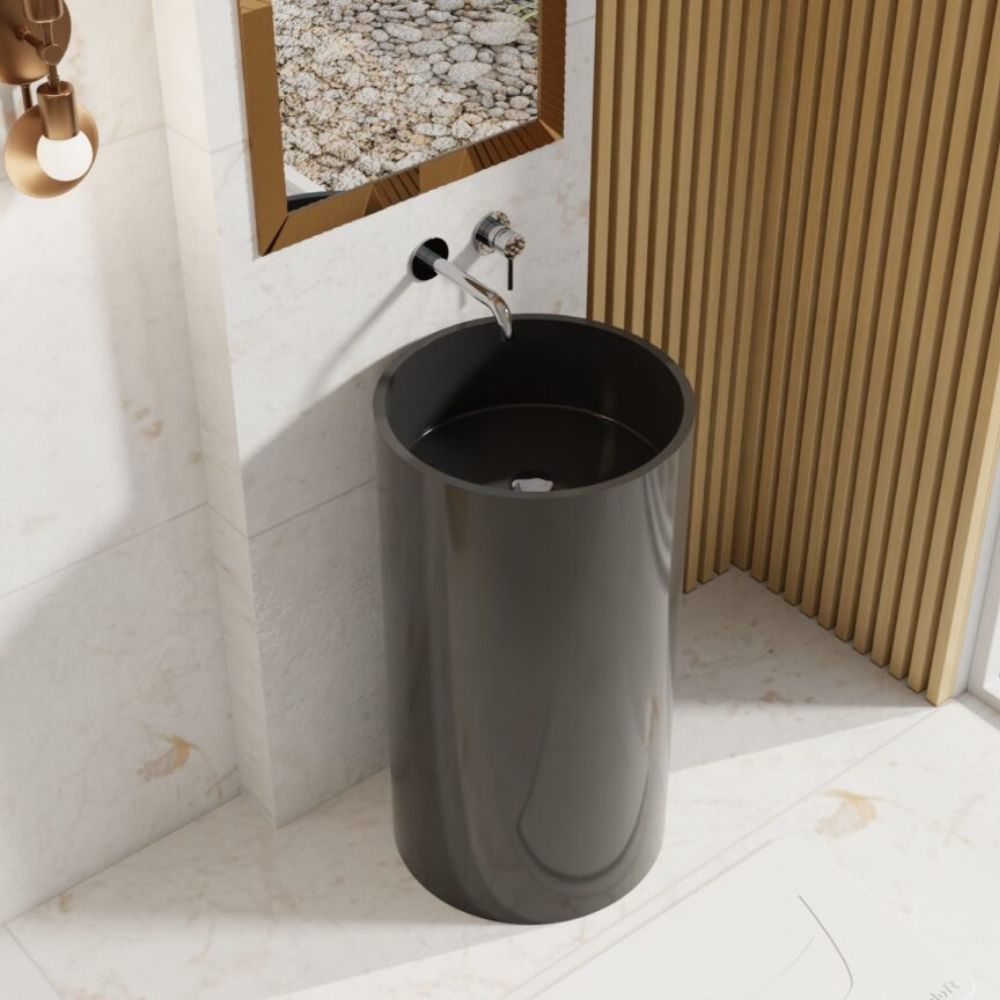 A modern dark gray cylindrical pedestal sink with a chrome faucet, set in a bathroom with white marble walls and floor, and a light wood slatted screen in the background.