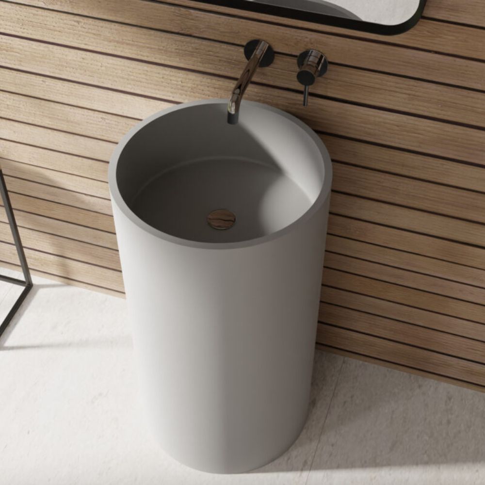 A matte gray cylindrical pedestal sink with a wall-mounted faucet, set against a light wood slat wall and light floor.