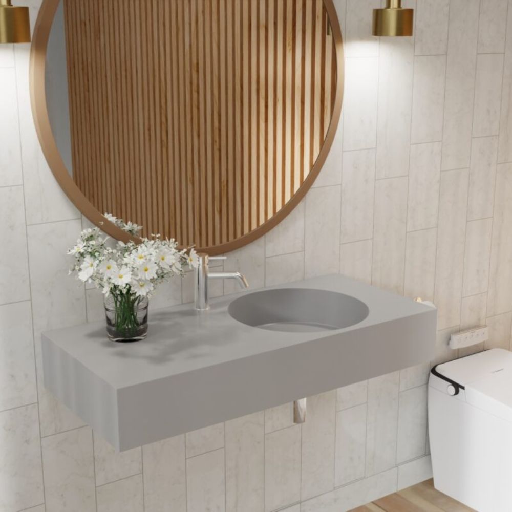 Bathroom with a concrete sink, round wooden mirror, and white flowers.