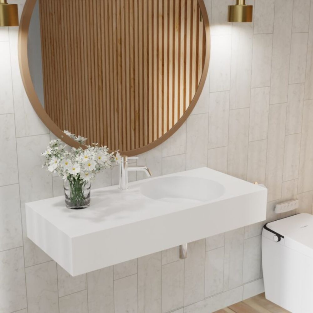 Bathroom with round wooden mirror, white sink, and flowers on a tiled wall.