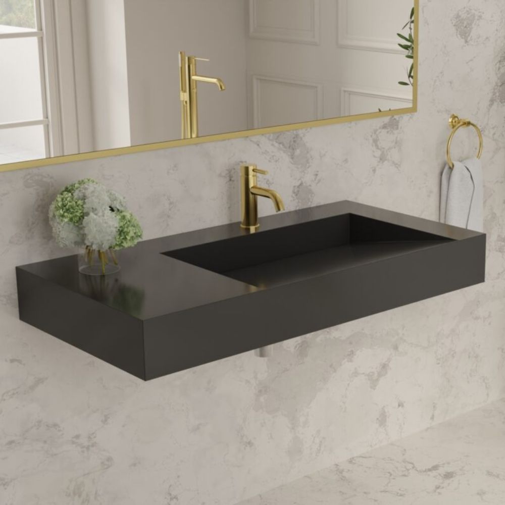 Bathroom vanity with black basin and gold faucet against a marble wall.