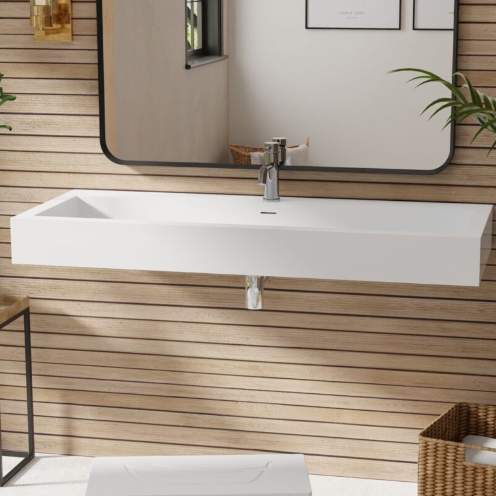 A modern white rectangular wall-mounted bathroom sink with a chrome faucet, shown against a light wood slat wall beneath a large black-framed mirror.