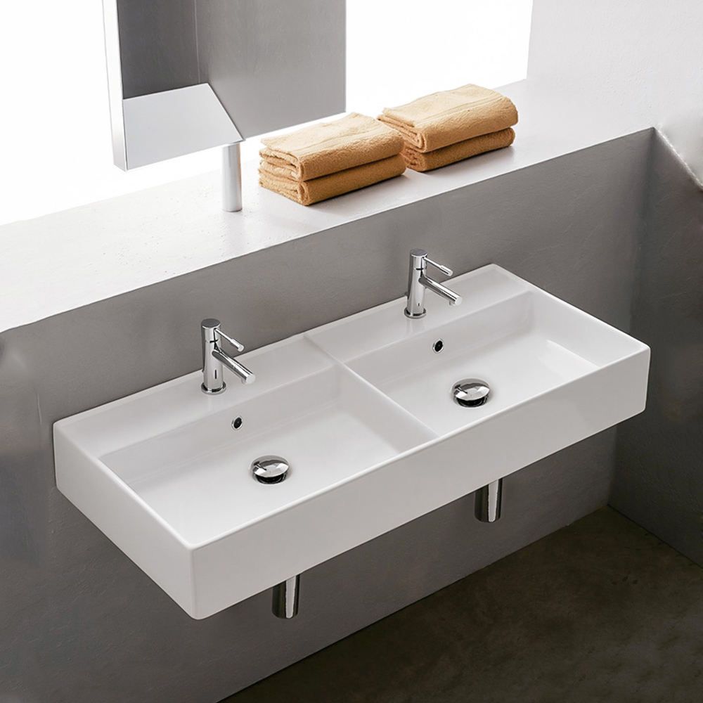 Bathroom sink with two faucets and towels on a shelf above.