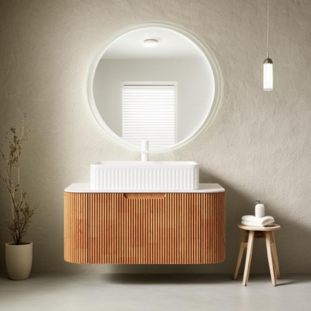Bathroom vanity with wooden cabinet, round mirror, and small stool with towels.